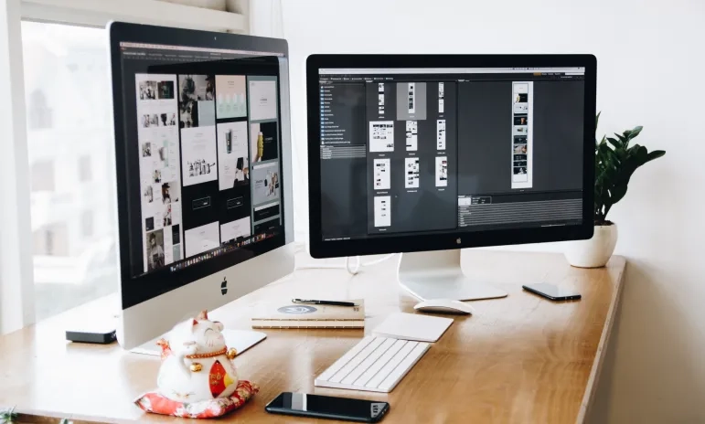 Web design checklist displayed across dual monitors on a designer's desk
