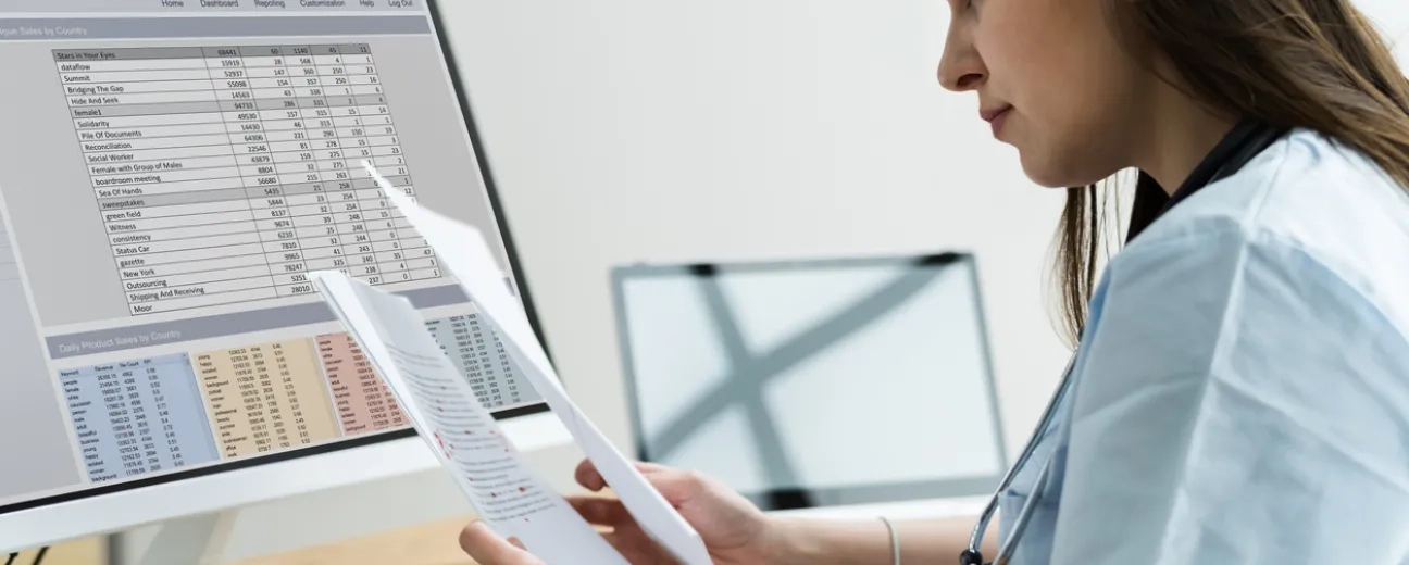 person in front of computer with medical bill codes and spreadsheets