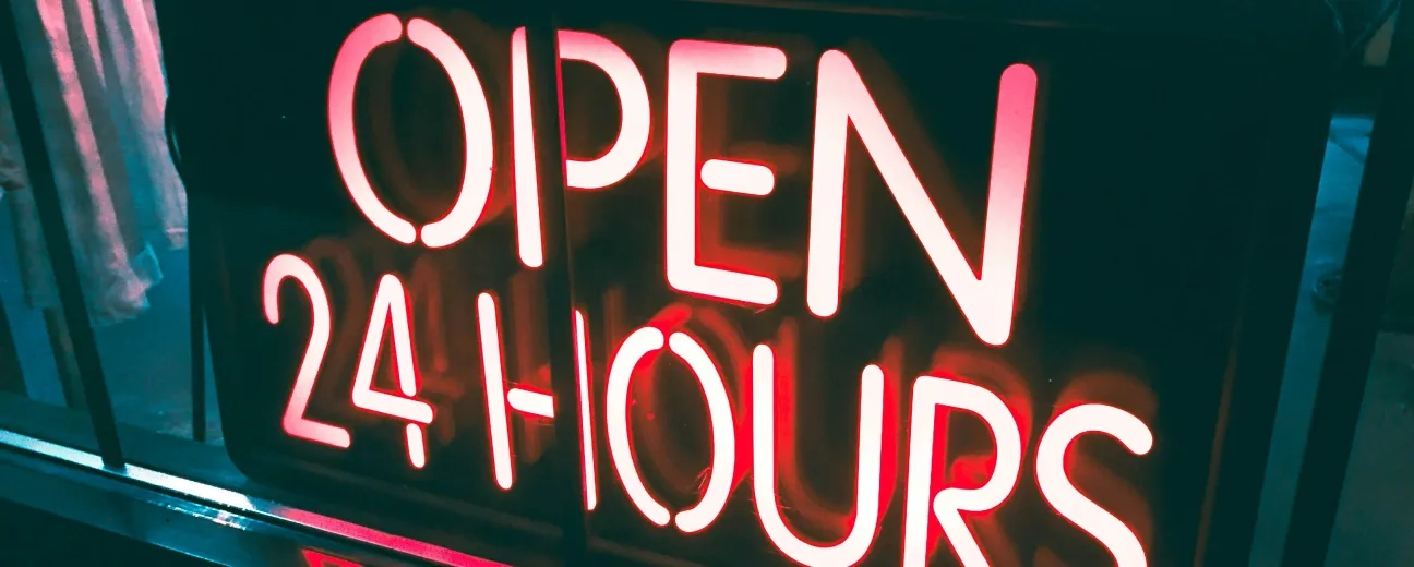 Neon sign that reads "OPEN 24 HOURS" hanging in a storefront window.
