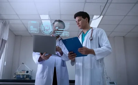 Two healthcare professionals reviewing patient data on a laptop with AI interface overlays in a clinical setting.