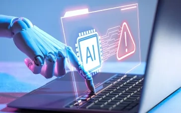 Robotic hand typing on a laptop with a glowing AI chip and warning sign hologram illustrating cybersecurity threats